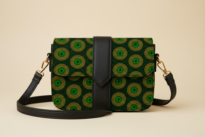 A black crossbody shoulder bag with a green and yellow circular shweshwe patterned fabric body, a black faux-leather strap, and gold-tone hardware