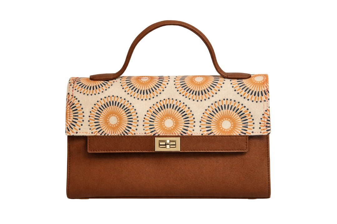 A structured handbag with a brown leather base and handle, featuring a cream-colored flap decorated with a repeating orange and navy geometric sunburst pattern, and a gold-tone turn-lock clasp on the front.